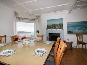 A dining room with a large table set for four, a fireplace, and two paintings on the walls.