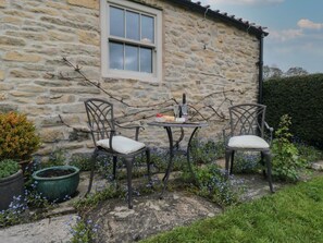 A stone building with a window, two chairs, a table, and potted plants.