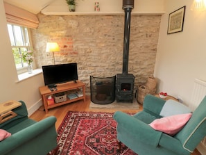 A cozy living room with a stone wall, a fireplace, a television, and teal armchairs.