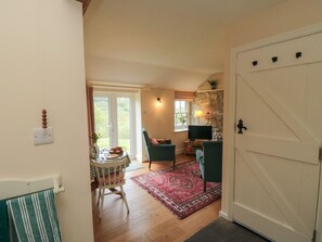 A room with a wooden floor, a dining table with chairs, a red rug, a television, and a stone wall.