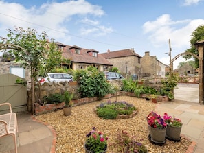 Un jardin avec un mur de pierres, des plantes en pot et un banc.