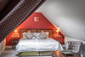 A bedroom with a sloped ceiling, a bed with white linens, two bedside lamps, and a red accent wall. - Prince's Cottage, Moniaive (Thornhill)