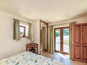 A bedroom with a bed, a desk, a mirror, and a sliding glass door leading to an outdoor area. - Routster Cottage, Settle (Settle)