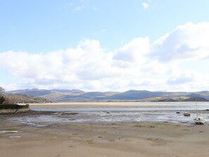 Eine Küstenlandschaft mit Sandstrand, einem kleinen Boot und sanften Hügeln unter einem teils bewölkten Himmel.