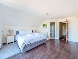 A bedroom with a large bed, a nightstand, a radiator, and a door leading to another room. - The Linhay, Washford (Watchet)