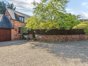 A stone building with a wooden fence, gravel driveway, and a tree with yellow leaves. - The Linhay, Washford (Watchet)