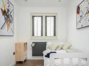 Un dormitorio con cama blanca, un radiador, una ventana con persianas, un armario de madera y dos cuadros abstractos en las paredes.