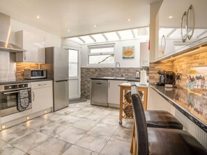 A modern kitchen with stainless steel appliances, a wooden backsplash, and a view of the city through a window. - Captiva Cottage, Saundersfoot (Saundersfoot)