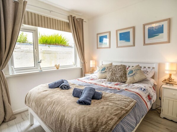 A bedroom with a bed, curtains, a window, bedside lamps, and framed pictures on the wall. - Captiva Cottage, Saundersfoot (Saundersfoot)