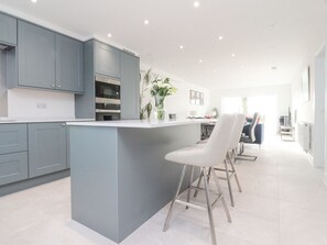 A modern kitchen with grey cabinets, a central island, and bar stools. - Apple Tree Cottage, Goosnargh. (Preston)