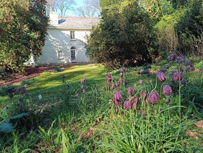 A white building with a garden in front, surrounded by trees and shrubs.