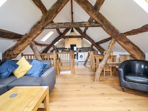 Una habitación estilo loft con vigas de madera a la vista, un sofá gris, un sillón de cuero negro y una mesa de madera.