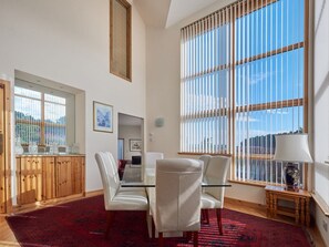 Una habitación amplia con un gran ventanal, una zona de comedor con una mesa de cristal y un aparador de madera.