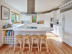 Una cocina moderna con armarios blancos, una isla central con taburetes y un refrigerador grande.