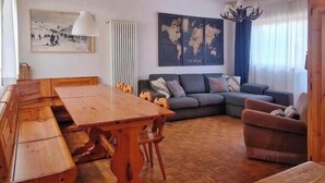 A living room with a wooden dining table, a sofa, and a chair. There is a world map on the wall and a chandelier. - Casa Polsa 1964 (Polsa)