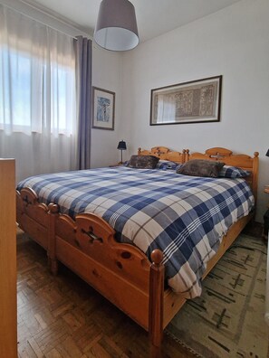 A wooden bed with a checkered bedspread, a nightstand, a lamp, and two framed pictures on the wall. - Casa Polsa 1964 (Polsa)