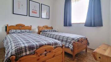 A room with two wooden beds, a ceiling light, and three framed pictures on the wall.