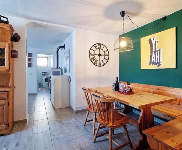 A dining area with a wooden table and chairs, a wall clock, and a green wall with a 'YEAH' sign. - Casa Polsa 1964 (Polsa)