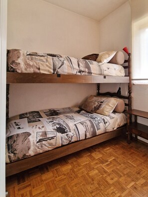 A bunk bed with a patterned bedspread and pillows, wooden flooring, and a window with curtains. - Casa Polsa 1964 (Polsa)