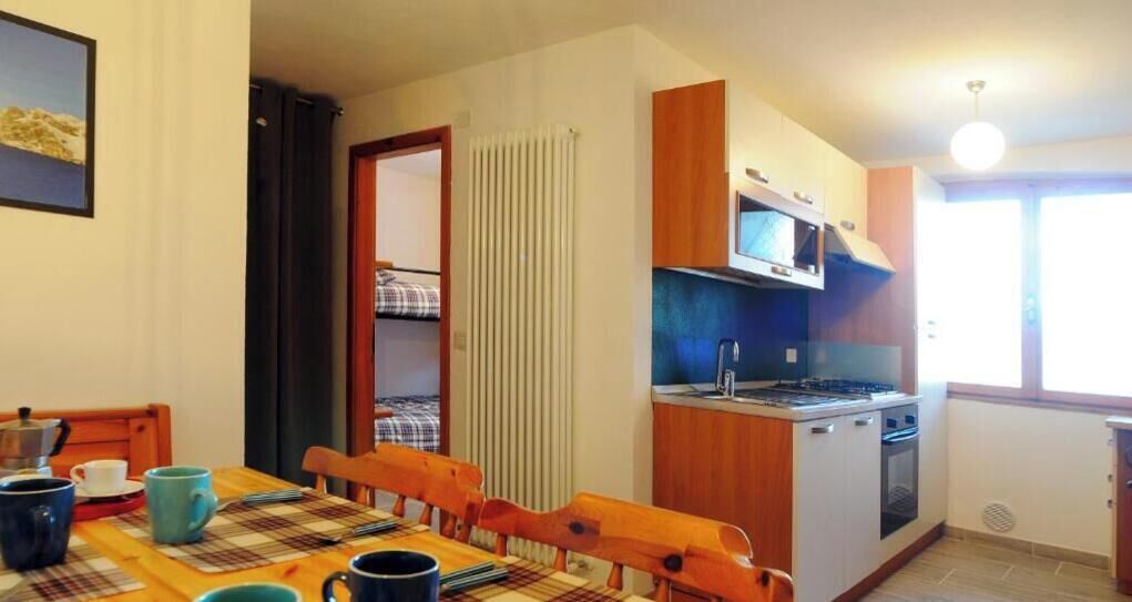 Cocina compacta con microondas, estufa y un pequeño comedor con mesa y sillas.