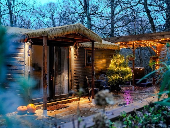 A rustic wooden cabin with a thatched roof, a porch, and string lights.