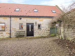 A stone building with a red-tiled roof, a black door, and a bench outside. - Charming Mill House Retreat (Whitby)