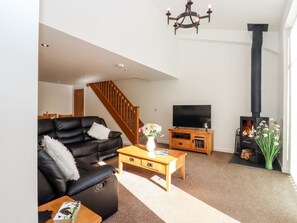 A living room with a sofa, coffee table, TV stand, fireplace, and a staircase. - The Milking Parlour, Cranbrook (Cranbrook)