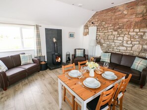 A cozy living room with a fireplace, a dining table set for four, and a stone wall. - Dairy Cottage, Whitland, Wales (Whitland)