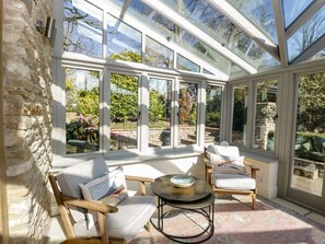 A conservatory with stone walls, large windows, and a seating area with chairs and a table. - Rose Cottage, Corsham, Wiltshire (Corsham)