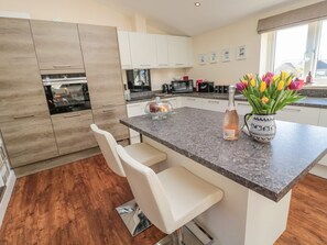 A modern kitchen with a central island, bar stools, a microwave, and a vase of tulips. - Cushat House, Embleton (Alnwick)