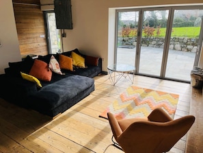 A living room with a sofa, a glass table, and a view through a sliding glass door to an outdoor area.