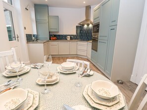 A dining area with a table set for four, a kitchen in the background, and light blue cabinets. - Sunnymede: Charming Home in Silsden (Keighley)