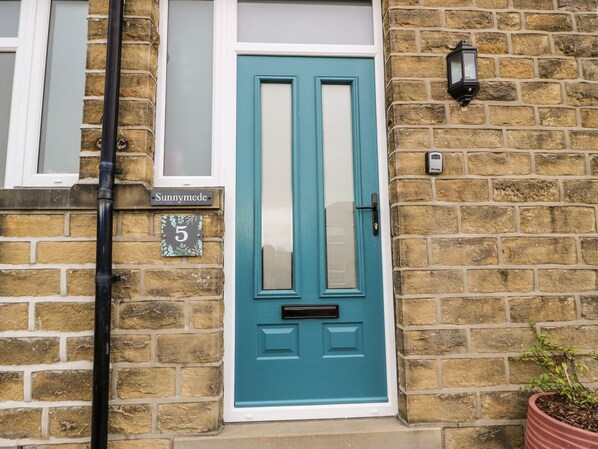 A turquoise door with a white frame, a brick wall, a small potted plant, and a street sign reading 'Sunnymede 5'. - Sunnymede: Charming Home in Silsden (Keighley)