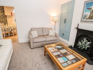 A living room with a beige sofa, a glass-top coffee table, a blue wardrobe, and a fireplace. - Sunnymede: Charming Home in Silsden (Keighley)