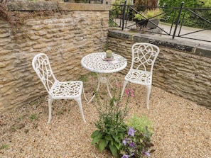 A stone wall, two white metal chairs, a round table with a cup, and a potted plant with purple flowers. - Snowdrop Cottage, Brompton-By-Sawdon (Scarborough)