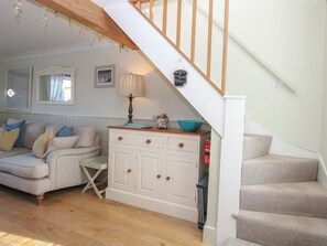 A living room with a sofa, a small table, a cabinet, and a staircase. - Herbies Cottage, Snettisham (King's Lynn)