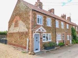 A two-story house with a stone facade, a white door, and a small porch. - Herbies Cottage, Snettisham (King's Lynn)