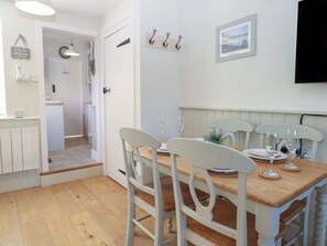A dining area with a wooden table and white chairs, a kitchen in the background, and a framed picture on the wall. - Herbies Cottage, Snettisham (King's Lynn)