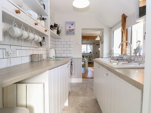 A narrow kitchen with white cabinets, a wooden countertop, and a view into the dining area. - Herbies Cottage, Snettisham (King's Lynn)