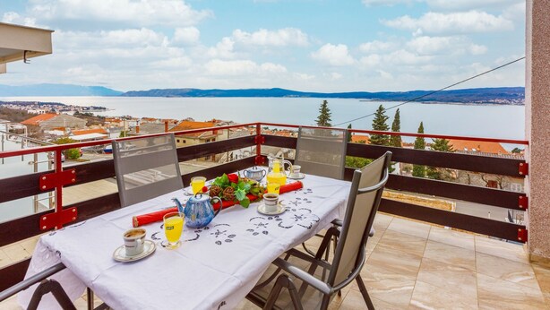 Ein Balkon mit Tisch für zwei Personen, mit Blick auf ein Gewässer und eine entfernte Landschaft.