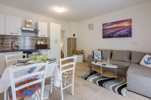 A modern kitchen with white cabinets, a dining table set with plates and cutlery, a sofa, and a painting of a lavender field on the wall. - Apartment with beautiful terrace, sea view and barbecue (Crikvenica)