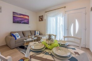 A dining area with a table set for two, a sofa, a small side table, and a painting on the wall. - Apartment with beautiful terrace, sea view and barbecue (Crikvenica)