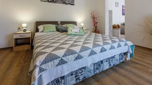 Ein Schlafzimmer mit Bett, Nachttischen, einem Wandbild und einer Tür zu einem anderen Raum.