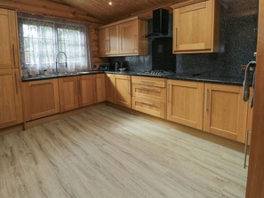 A wooden cabin-style kitchen with a large window, a stove, and a sink.
