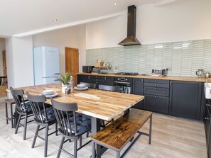 A modern kitchen with a wooden table, black chairs, a built-in oven, and a black range hood. - Cooper's Rest (Gorffwysfa Coopers), Dolwyddelan (Dolwyddelan)