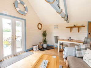 A cozy living area with a wooden floor, a sofa, a coffee table, a dining table, and a chair. There is a potted plant and a wall-mounted shelf with decorative items. - Charming The Nook Retreat in Louth (Louth)