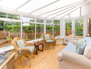 A conservatory with wicker furniture, a cushioned sofa, and a wooden table. - Estuary View, Warkworth (Morpeth)