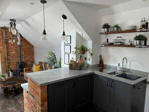 Una cocina con pared de ladrillo decorativa, una isla central, armarios negros y una lámpara colgante.