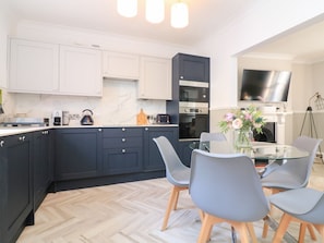 A modern kitchen with dark cabinets, a glass dining table, and a TV mounted above it.