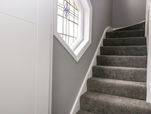 A carpeted staircase with a white wall and a window with a stained glass design. - Park View Upper, in Llandudno. (Llandudno)